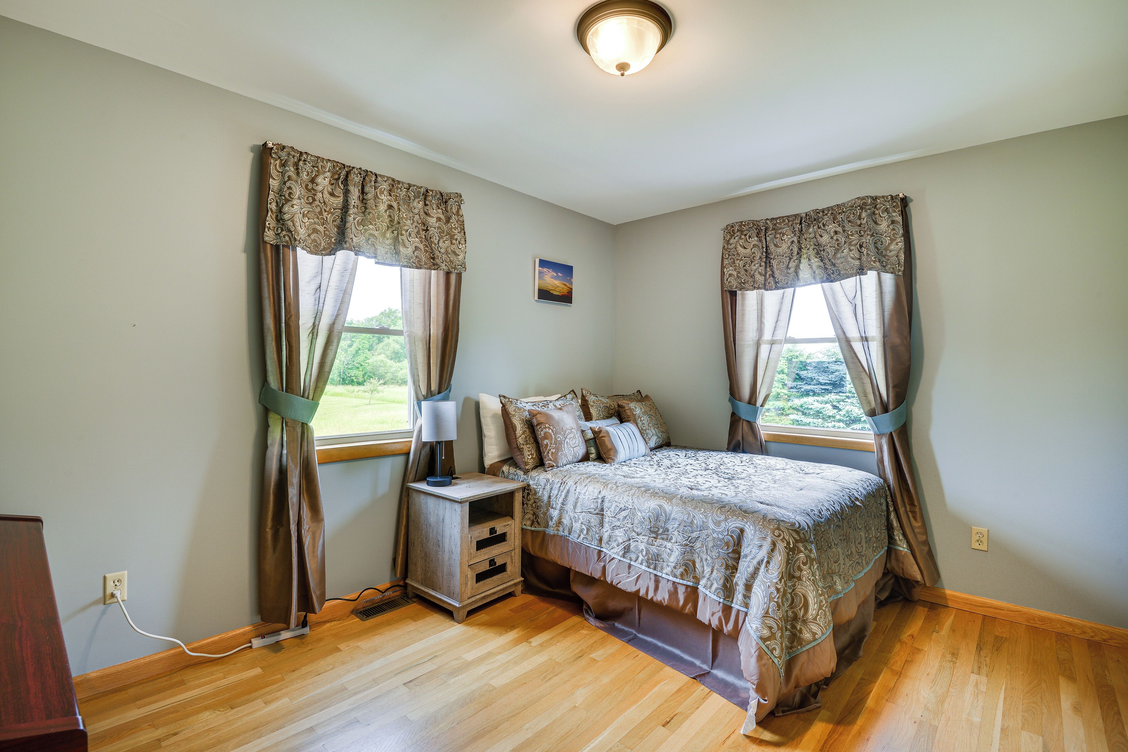 A bedroom with a large bed, two bedside tables, a nightstand, and a window with curtains.