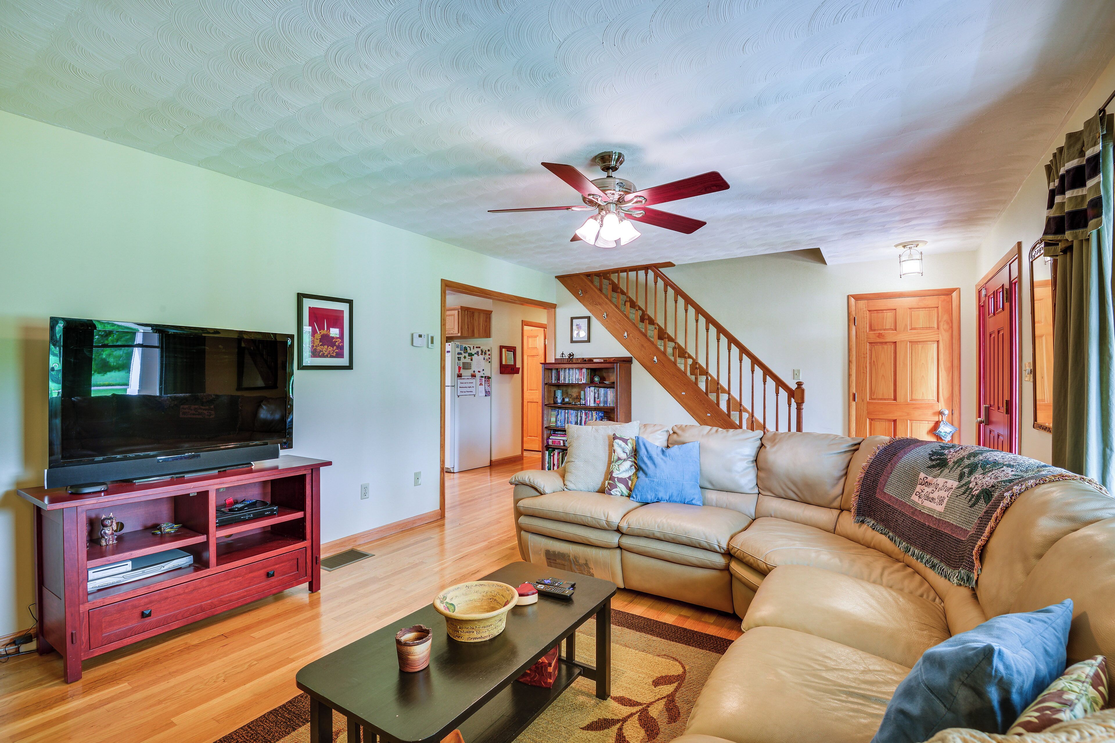 A living room with a television on a wooden stand, a leather sofa, a wooden coffee table, and a ceiling fan.