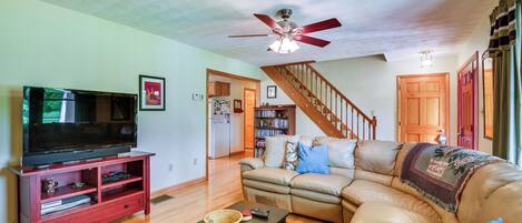 A living room with a television on a wooden stand, a leather sofa, a wooden coffee table, and a ceiling fan.