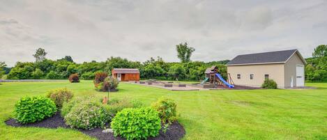 A grassy area with a playground, a building with a gray roof, and a small red-roofed structure.