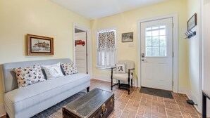 A living room with a sofa, a chair, a wooden chest, and a door.