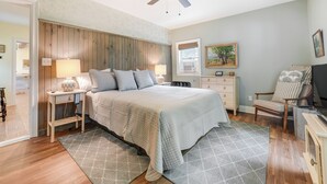 A bedroom with a bed, bedside tables, a chair, a desk, a ceiling fan, and a window.