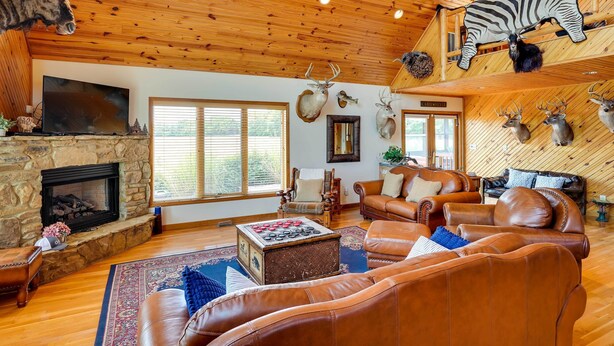 Ein gemütliches Wohnzimmer mit Ledersofas, einem Kamin aus Stein, aufgehängten Tierköpfen und einer Holzbalkendecke.