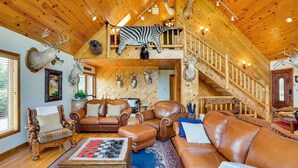 Ein Holzhütten-Interieur mit Schlafzimmer-Loft, Ledermöbeln und Hirschgeweihen an den Wänden.