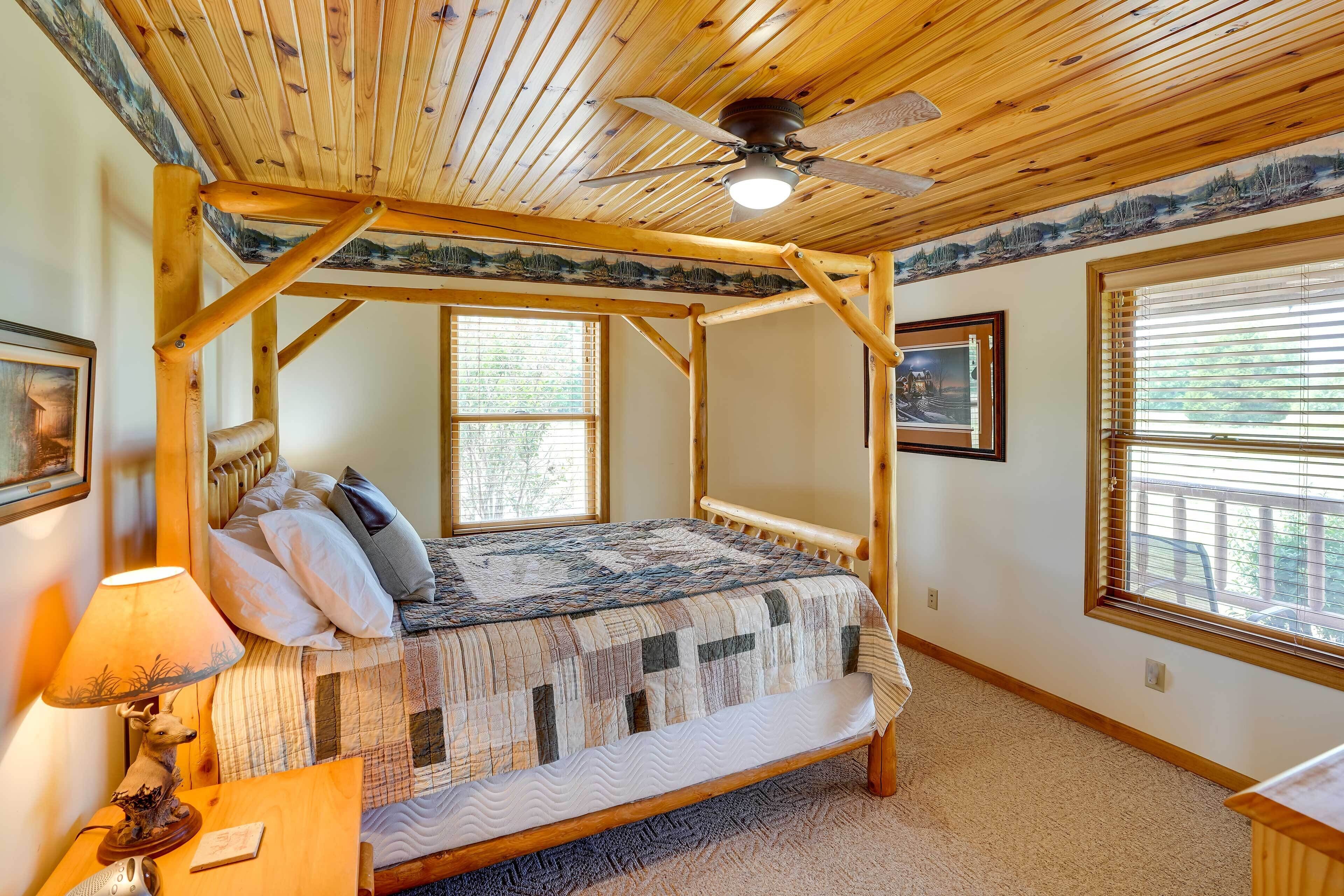 A wooden four-poster bed with a quilt, a ceiling fan, and a window with blinds.