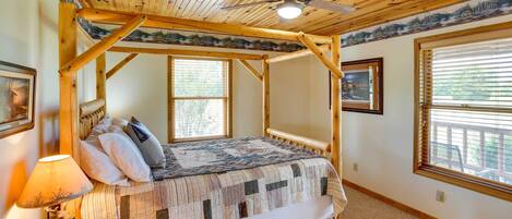 A wooden four-poster bed with a quilt, a ceiling fan, and a window with blinds.