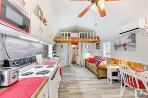A compact kitchen with a stove, microwave, and toaster. There is a dining area with a table and chairs, and a loft bedroom with a bed and window. - Paris Vacation Rental ~ 22 Mi to Mount Magazine! (Paris)