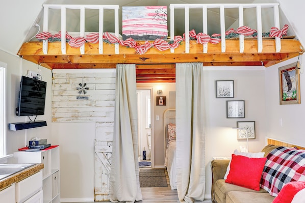 A cozy room with a loft bed, a television, a wooden dresser, and a red and black checkered blanket on a sofa. - Paris Vacation Rental ~ 22 Mi to Mount Magazine! (Paris)