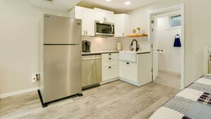 A compact kitchen with white cabinets, a stainless steel refrigerator, a microwave, and a dishwasher. - Missouri Studio Getaway: Close to Parks & Hiking (Liberty)