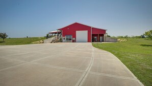 Un bâtiment rouge avec un grand portail de garage, une allée couverte et un espace verdoyant avec des arbres.
