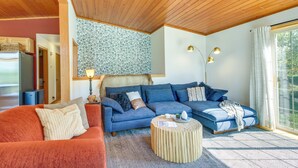 A cozy living room with a wooden ceiling, a blue sofa set, a red sofa, and a patterned rug.