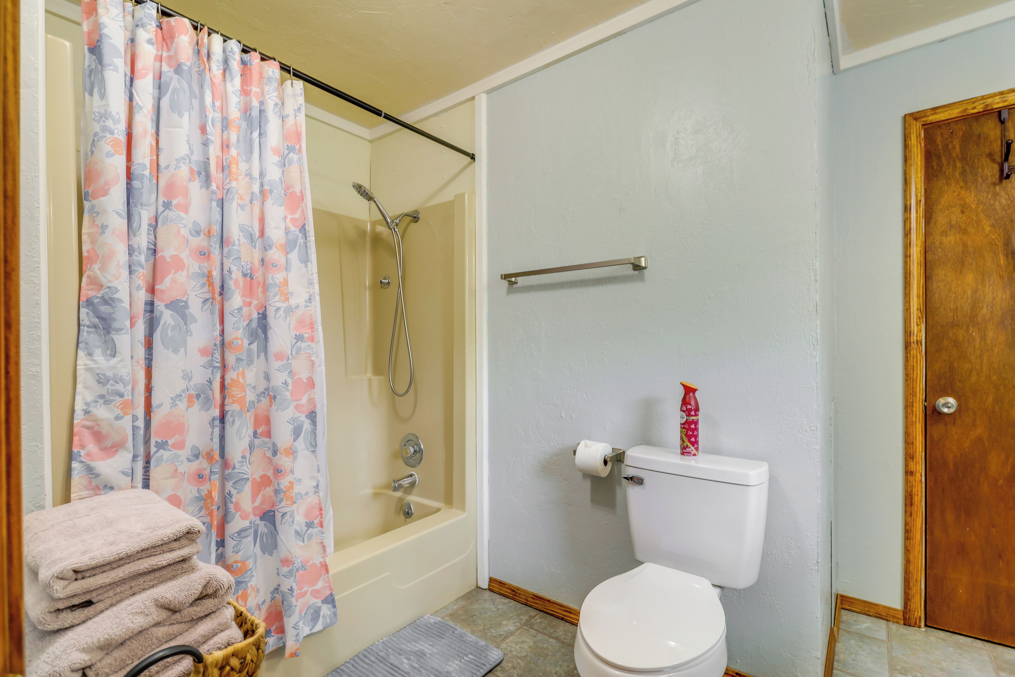 A bathroom with a shower, toilet, and a stack of towels.