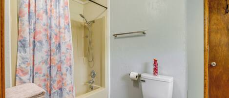 A bathroom with a shower, toilet, and a stack of towels.