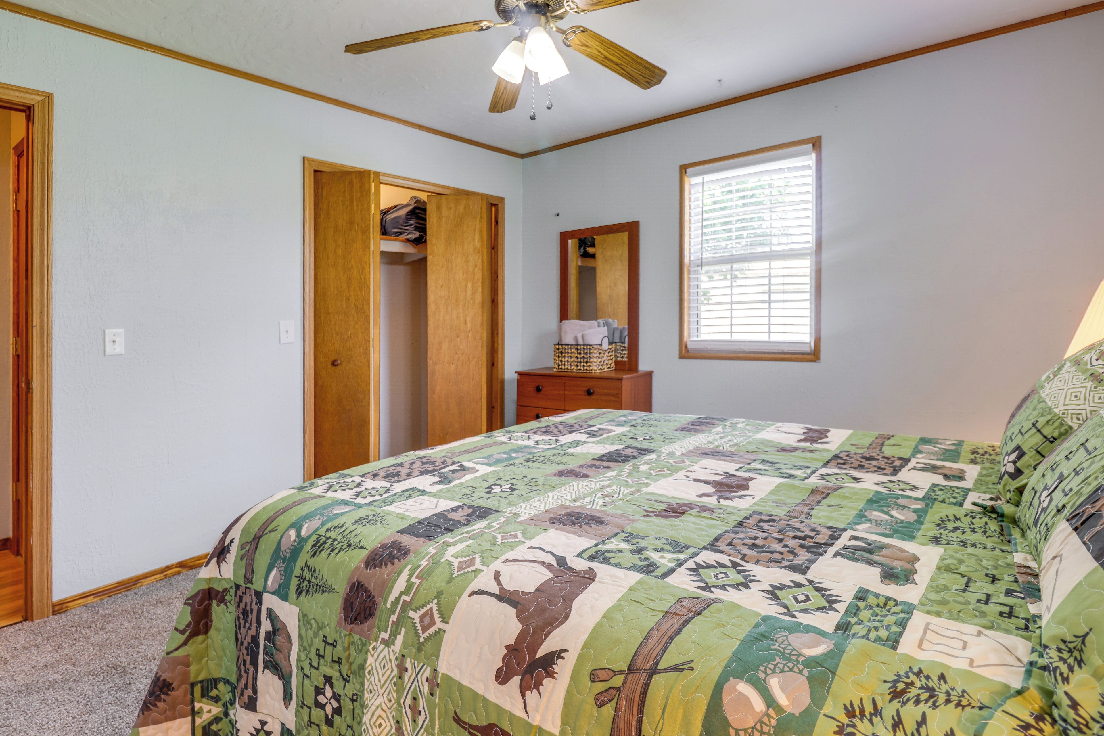 A bedroom with a bed, a ceiling fan, a window with blinds, a dresser, and a closet.