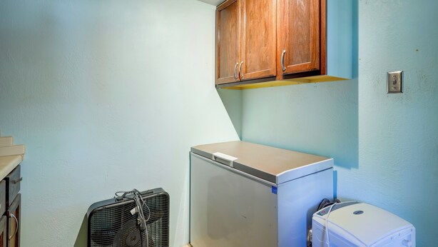 Une petite pièce équipée d’un réfrigérateur, d’un ventilateur et d’armoires en bois.