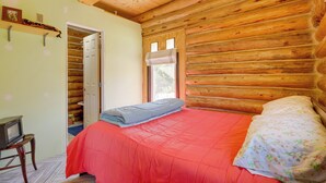 Une chambre à coucher aménagée dans une cabane en rondins, avec un lit, une petite table et une porte donnant sur un placard.