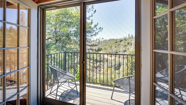 Ein Balkon mit Metallstühlen und einer Holzterrasse, mit Blick auf eine bewaldete Gegend.