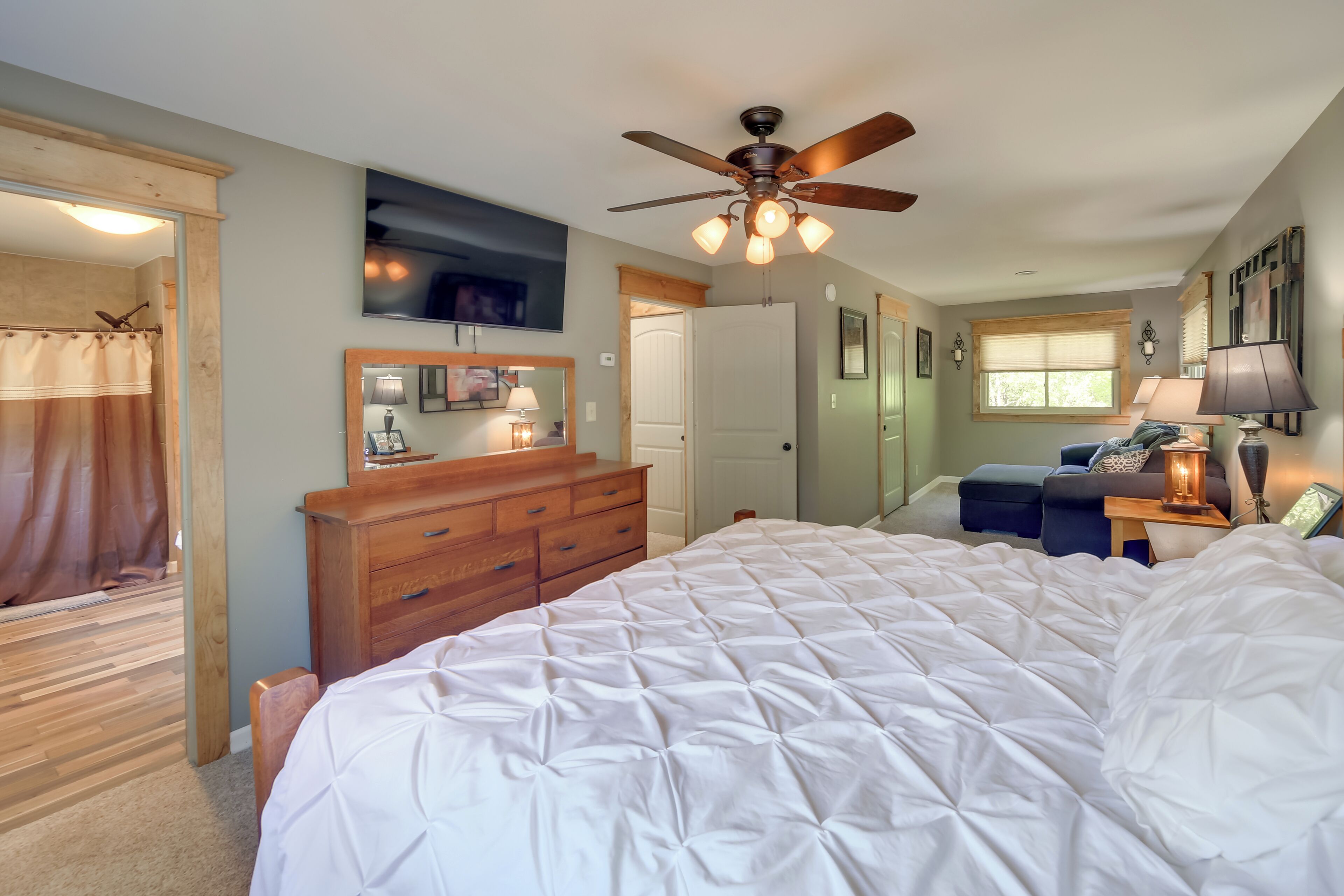 A bedroom with a large bed, wooden dresser, ceiling fan, and a window with blinds.