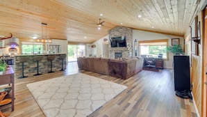 A spacious living area with a stone fireplace, wooden ceiling, and a large TV.