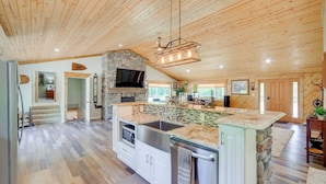 A spacious kitchen with a stone island, stainless steel appliances, and a large TV.