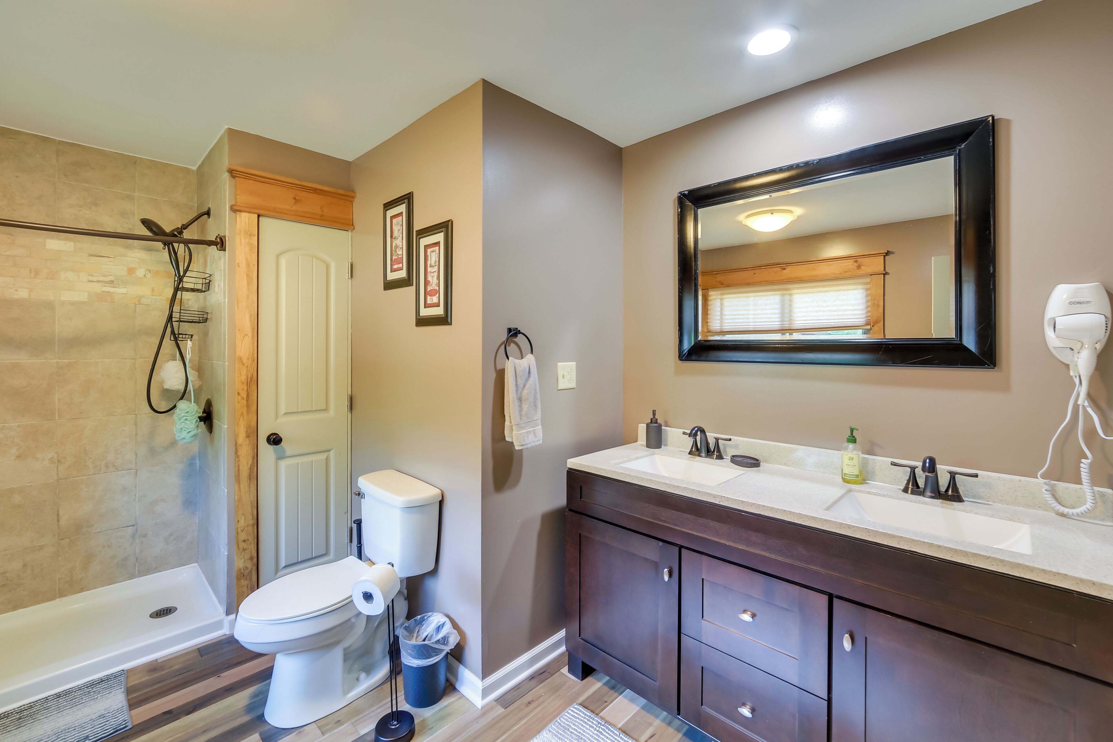 A bathroom with a shower, toilet, vanity, and a large mirror.