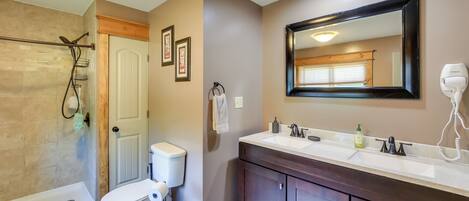 A bathroom with a shower, toilet, vanity, and a large mirror.