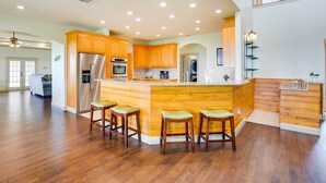 A spacious kitchen with wooden cabinets, a stainless steel refrigerator, and a central island with bar stools. - The Oasis Ranch 20-acre Ranch in Whitewright! (Whitewright)