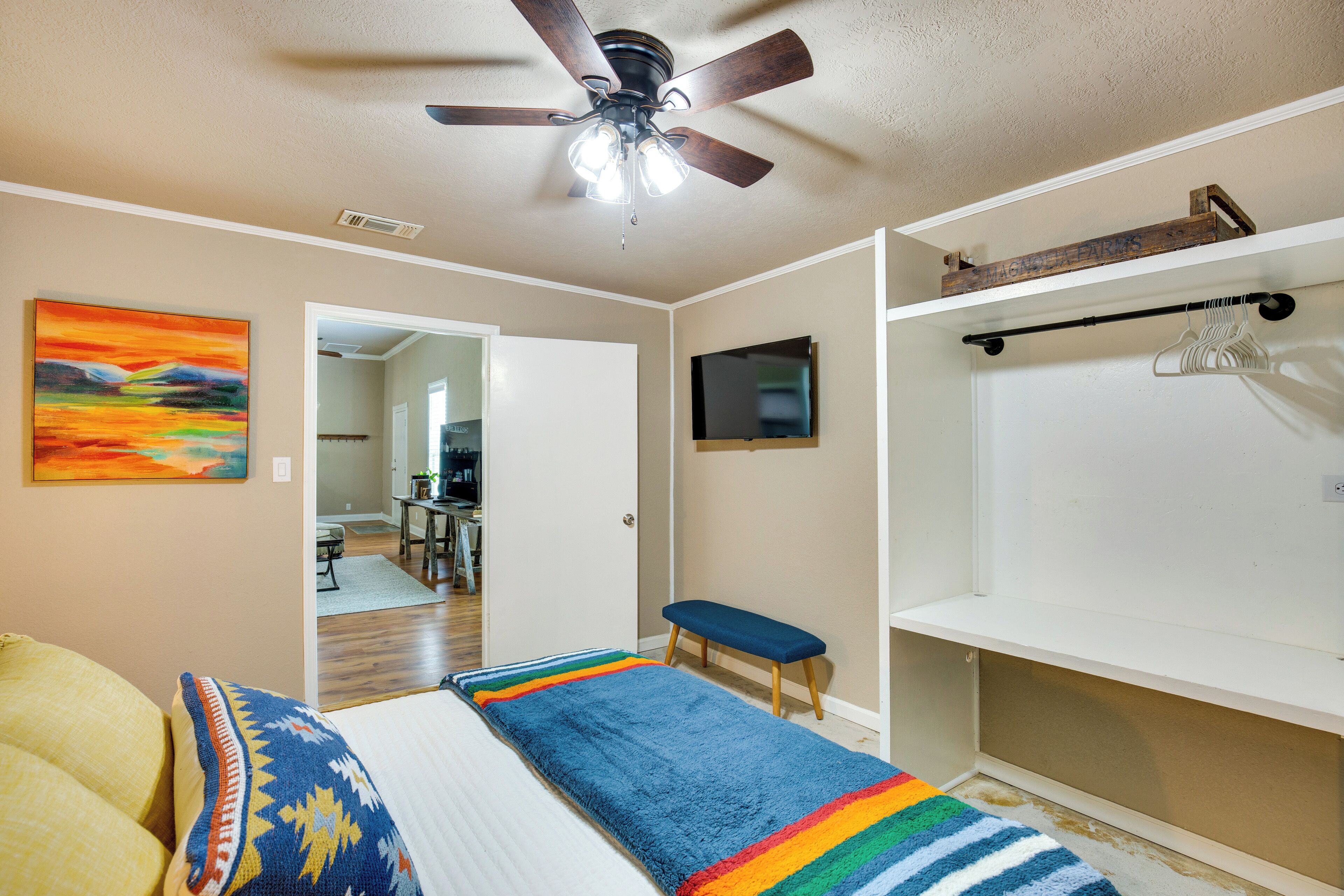 Un dormitorio con cama, ventilador de techo, televisor y banca.