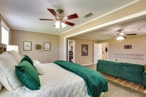 Quarto com cama, dois travesseiros verdes, um sofá verde e duas ventoinhas de teto.