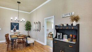 Zona pranzo con tavolo e sedie in legno, un lampadario e un angolo caffè con diversi accessori.