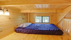 Ein Schlafzimmer einer Holzhütte mit Bett, Fenster und einer Lampe.