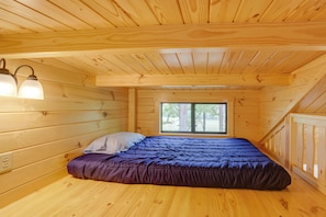 Ein Schlafzimmer einer Holzhütte mit Bett, Fenster und einer Lampe.