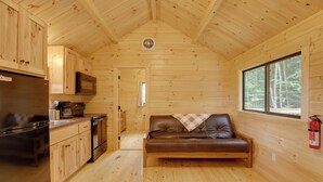 Ein Holzblock-Innenraum mit einer Küchenzeile, einem Ledersofa und einem Fenster mit Blick auf den Wald.