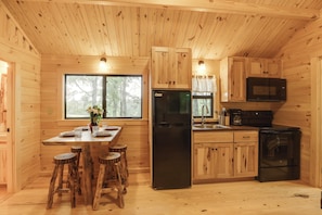 A wooden cabin kitchen with a central island, bar stools, a refrigerator, a microwave, and a stove. - Scenic Deck & Grill: Middlebury Center Retreat! (Osceola)