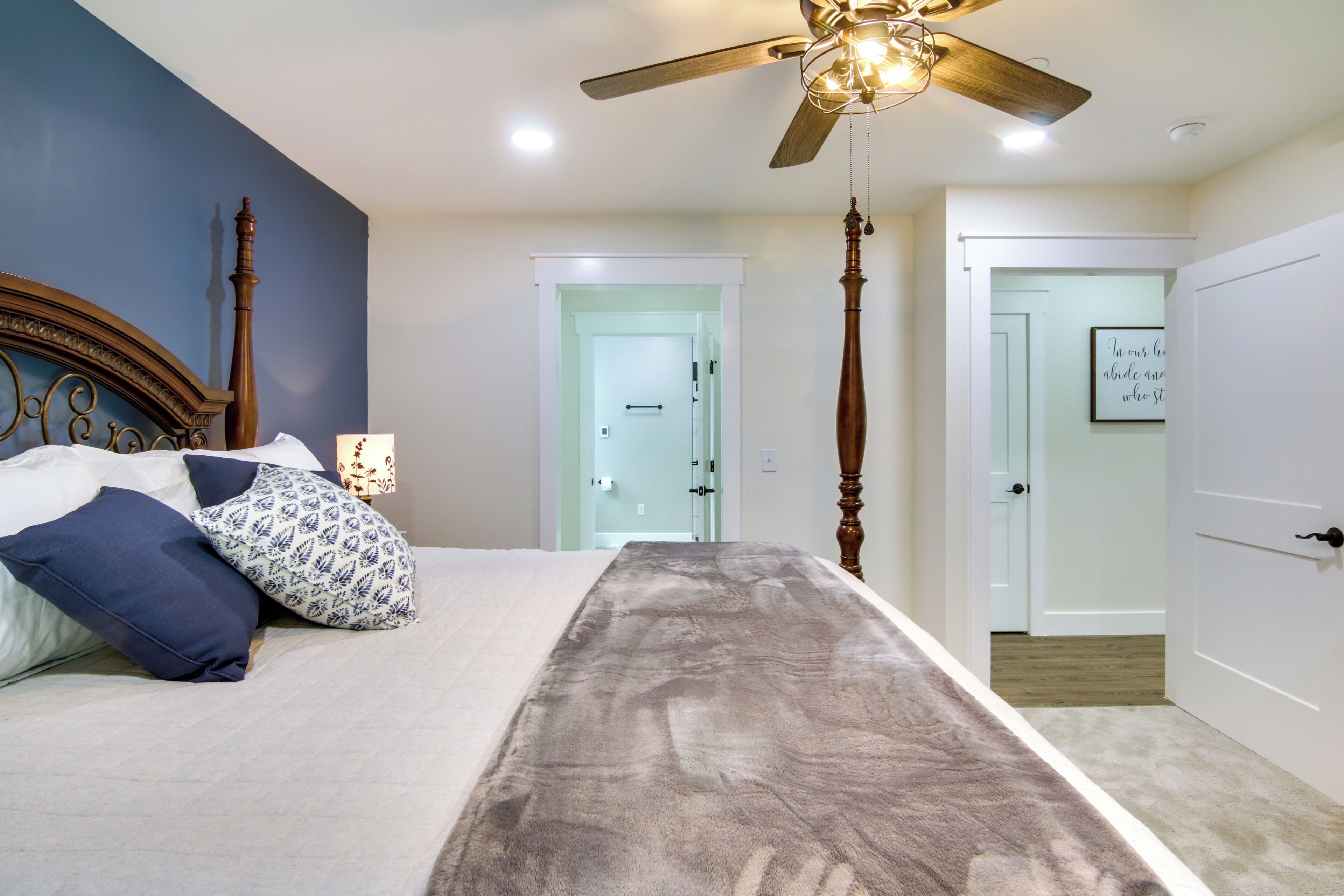 A bedroom with a bed, a ceiling fan, a nightstand, and a door leading to another room.