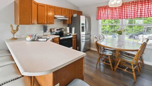 Une cuisine moderne avec des meubles en bois, un grand îlot central, des appareils électroménagers en acier inoxydable et un coin repas comprenant une table ronde et des chaises.