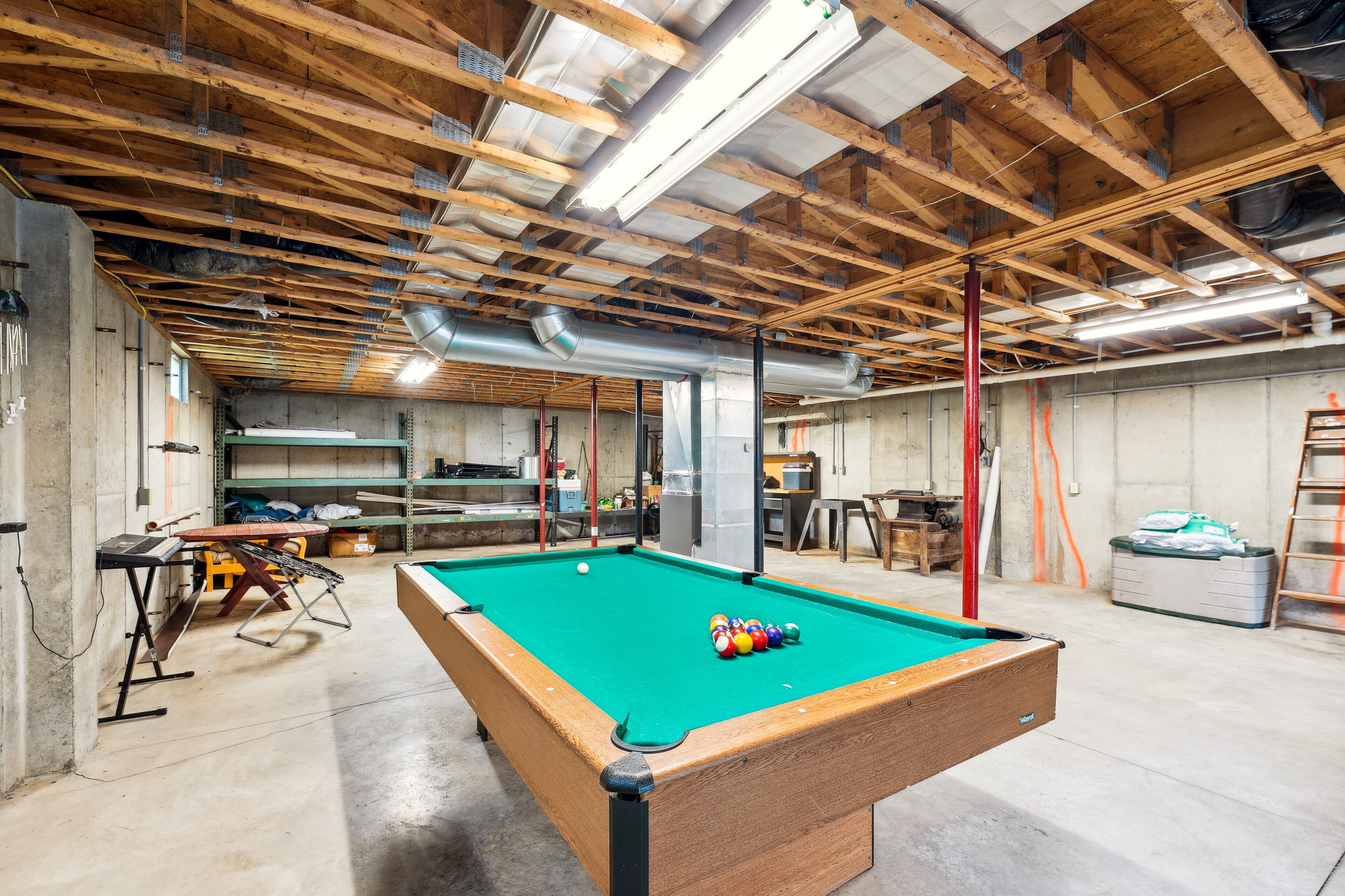 A pool table in a spacious room with exposed wooden beams and concrete walls.