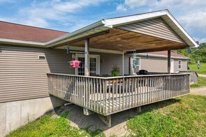 A covered deck with a wooden railing, a small porch area, and a grill. - 'heaven on the Hill' Retreat w/ Deck + Gas Grill! (Frewsburg)