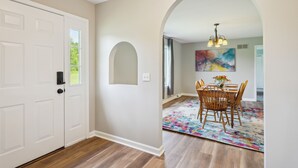 A hallway with a white door, wooden flooring, an arched doorway, a dining area with a table and chairs, and a colorful rug. - 'heaven on the Hill' Retreat w/ Deck + Gas Grill! (Frewsburg)
