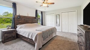 A bedroom with a bed, nightstand, dresser, ceiling fan, and a view of greenery outside. - 'heaven on the Hill' Retreat w/ Deck + Gas Grill! (Frewsburg)