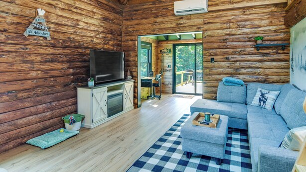 L’intérieur d’une cabane en rondins, avec un téléviseur posé sur un meuble, un canapé et un tapis à carreaux.