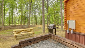 Una cabaña de madera con una parrilla y una mesa de picnic en un área boscosa.
