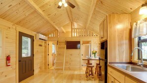 Interior de una cabaña de madera con área de cocina, pisos de madera y un ventilador de techo.
