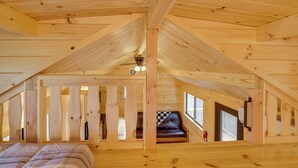 Un dormitorio rústico en el ático con techo inclinado, cama, sofá de cuero y ventana.