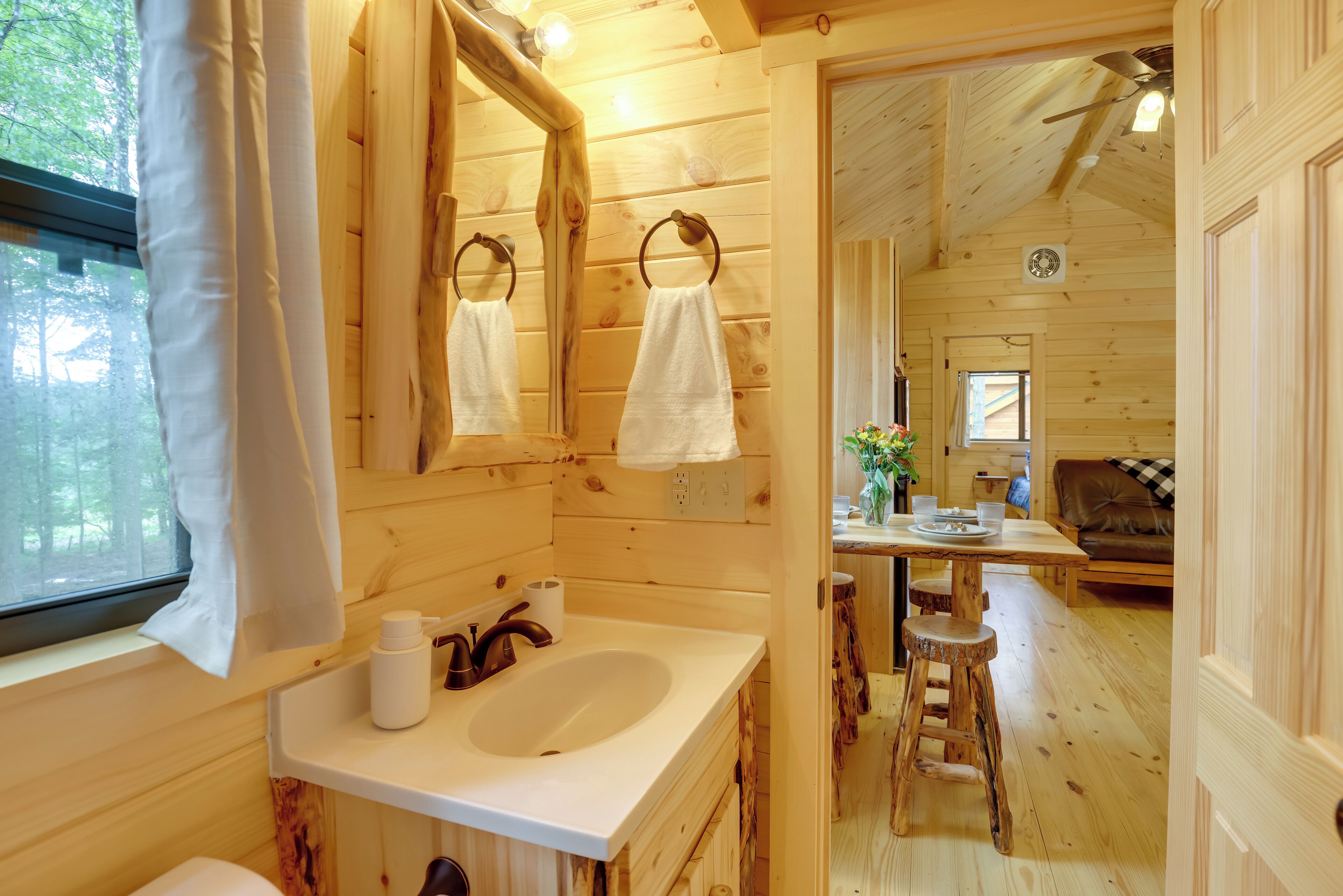 A wooden cabin interior with a bathroom featuring a sink, mirror, and towel rings.