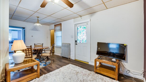 A living room with a wooden floor, a white rug, a television on a wooden stand, a lamp on a side table, and a ceiling fan. - Bath Vacation Rental Condo w/ Pool Access! (Bath)