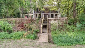 Eine hölzerne Treppe führt zu einem mehrstöckigen Gebäude, das von dichtem Wald umgeben ist.