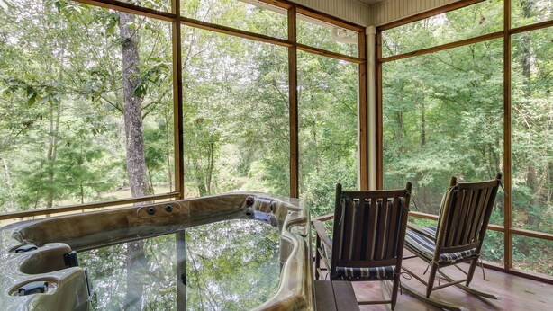 Ein Whirlpool mit Glasverkleidung, eine Holzterrasse und zwei Schaukelstühle mit Blick auf den Wald.