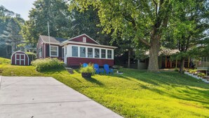 A house with a red exterior and white trim, a front yard with green grass, a concrete driveway, and two blue chairs in the yard. - Delavan Retreat w/ Patio on Turtle Lake! (Delavan)