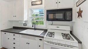 A kitchen with white cabinets, a granite countertop, a sink, a stove, a microwave, and a window with a view of greenery. - Delavan Retreat w/ Patio on Turtle Lake! (Delavan)